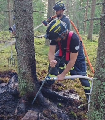 Brandman använder jordspett för att släcka glödbrand i skogsmark